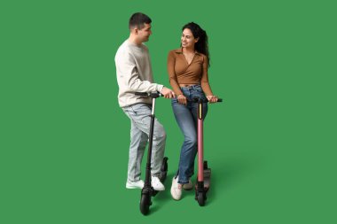 Yeşil arka planda modern elektrikli scooterları olan güzel genç bir çift.
