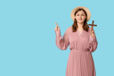 Ahşap haçı olan dindar genç bir kadın mavi arka plandaki bir şeyi işaret ediyor.