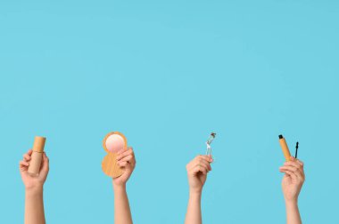 Mavi arkaplanda bigudi, fosforlu kalem, temel ve rimel olan kadın elleri