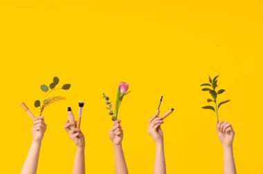 Lale, kapatıcı, temel, fırça, rimel ve sarı arka planda dalları olan kadın elleri