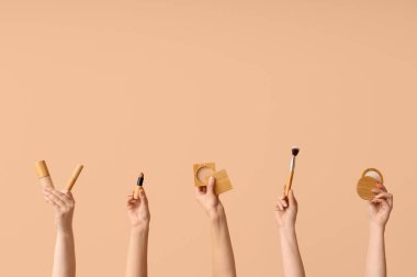 Ruj, temel, fosforlu kalem, rimel, kapatıcı ve bej arka planda fırça kullanan kadın elleri