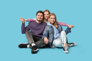 Mavi arka planda oturan şık kot elbiseli mutlu bir aile.