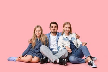 Pembe arka planda oturan şık kot elbiseli mutlu bir aile.