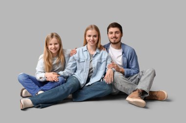 Gri arka planda oturan şık kot elbiseli mutlu bir aile.