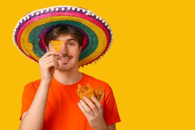 Sarı arka planda sombrero ve tortilla cipsi olan genç bir adamın portresi. Ulusal Tortilla Cipsi Günü kutlaması