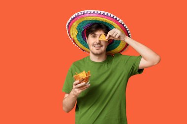 Sombrero ve turuncu arka planda tortilla cipsi olan genç bir adamın portresi. Ulusal Tortilla Cipsi Günü kutlaması