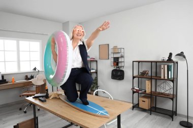 Yüzme yüzüğü ve sörf tahtası olan olgun bir iş kadını yaz tatiline ofiste hazır.