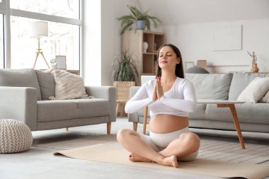 Sportif hamile kadın evde meditasyon yapıyor.