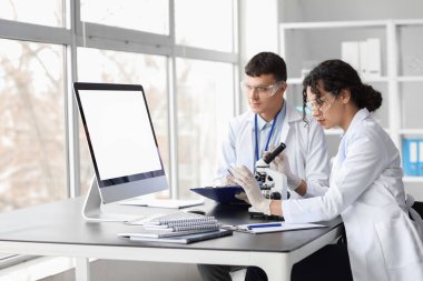 Laboratuvardaki masada mikroskopla çalışan genç kimyagerler.