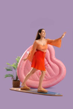 Sörf tahtası, avuç içi ve eflatun arka planda şişirilebilir şiltesi olan gülümseyen genç kadın.