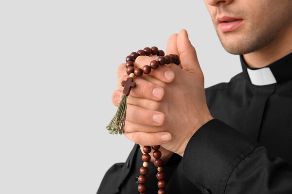 Young priest praying with beads on dark background, closeup