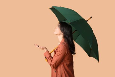 Bej arka planda şemsiyesi açık genç bir kadın.