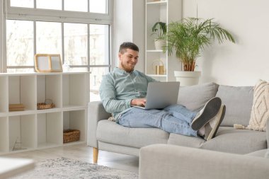 Genç sakallı adam evde dizüstü bilgisayar kullanıyor.