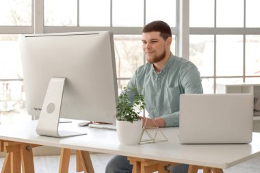 Genç sakallı adam evdeki masada bilgisayar kullanıyor.