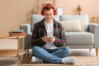 Genç adam sesli kitap dinliyor ve oturma odasında yerde oturuyor.