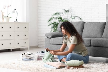 Güzel, genç, mutlu, Afro-Amerikan kadın. Temiz giysileri evde katlıyor.