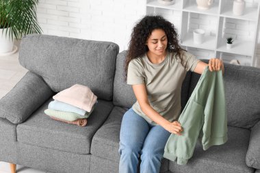 Güzel, genç, mutlu, Afro-Amerikan kadın. Temiz giysileri evde katlıyor.