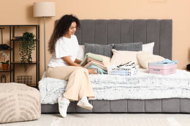 Güzel, genç, mutlu, Afro-Amerikan bir kadın yatak odasında temiz giysiler katlıyor.