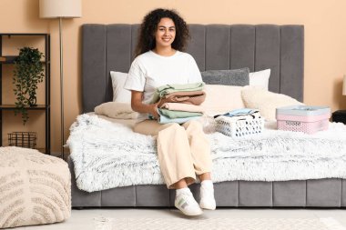 Güzel, genç, mutlu, Afro-Amerikan bir kadın yatak odasında temiz giysiler katlıyor.