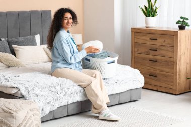 Güzel, genç, mutlu, Afro-Amerikan bir kadın. Yatak odasında temiz giysilerle dolu bir sepet.