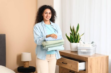 Güzel, genç, mutlu, Afro-Amerikan kadın. Yatak odasında bir yığın temiz giysi var.