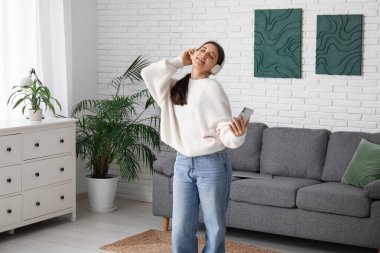 Oturma odasında kulaklıklı genç bir kadın siyah kanepenin yanında dans ediyor.