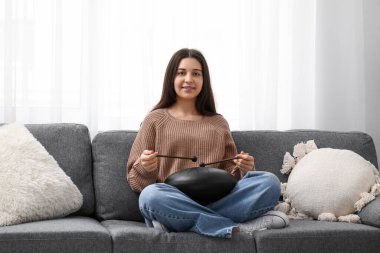 Oturma odasında siyah kanepede glukofon çalan genç bir kadın.