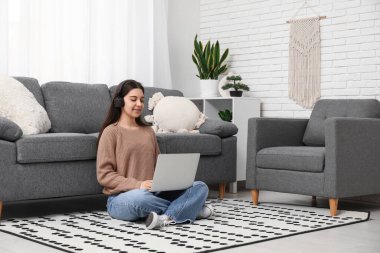 Oturma odasında dizüstü bilgisayar kullanan genç bir kadın.