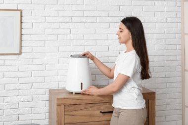 Genç bir kadın modern nemlendiriciyi şık bir odada ahşap çekmecelerde açıyor.