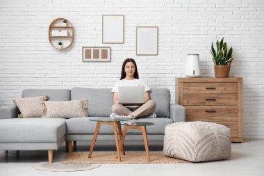 Genç bir kadın modern nemlendiricinin yanındaki rahat koltukta dizüstü bilgisayar kullanıyor.