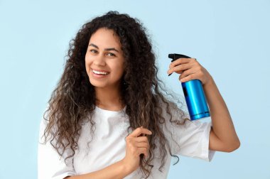 Mavi arka planda saç spreyi olan güzel, mutlu, Afro-Amerikalı bir kadın.