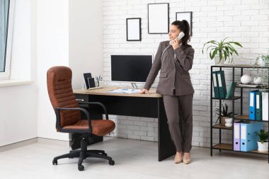 Kadın ofis çalışanı şık bir ofiste iş yerinin yakınında telefonla konuşuyor.