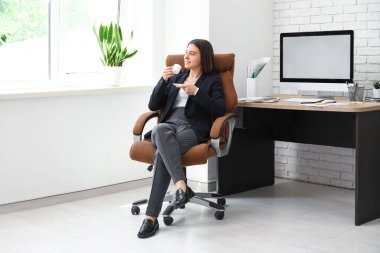 Kadın ofis çalışanı kahve içiyor ve işyerindeki koltukta oturuyor.