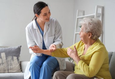 Fizyoterapist evde yaşlı bir kadına yardım ediyor.