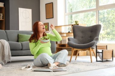 Bilgisayarlı hamile bir kadın evde taze sebze salatası yiyor.