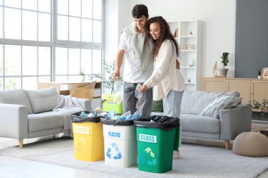 Genç bir çift evdeki çöp konteynırına plastik şişe atıyor. Atık sıralama kavramı