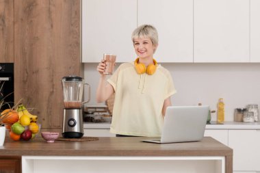 Mutfakta bir bardak meyve suyu ve blender ile genç ve sportif bir kadın.