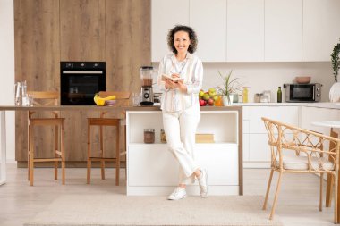 Not defteri ve blenderi olan olgun bir kadın mutfakta meyve püresi yapıyor.