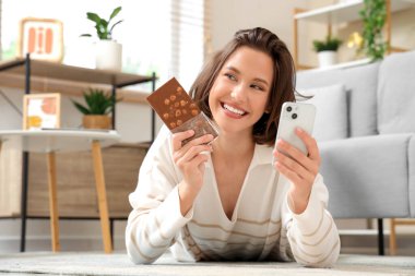 Lezzetli çikolatalı ve cep telefonlu genç ve güzel bir kadın evde yerde yatıyor.