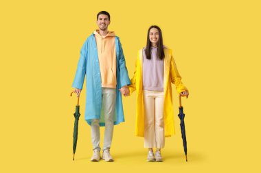 Sarı arka planda yağmurluk giyen genç çift.