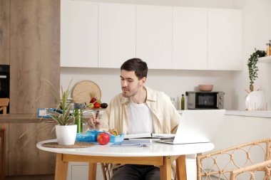 Beslenme çantalı genç adam mutfaktaki masada ders çalışıyor.