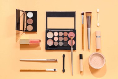 Turuncu zemin üzerinde kozmetik ürünler bulunan şık makyaj fırçaları