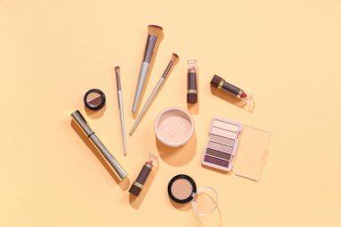 Turuncu zemin üzerinde kozmetik ürünler bulunan şık makyaj fırçaları