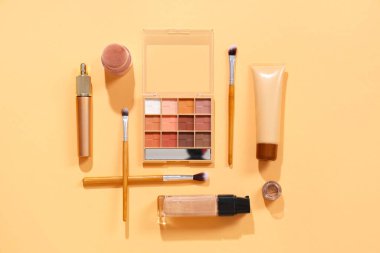 Turuncu zemin üzerinde kozmetik ürünler bulunan şık makyaj fırçaları