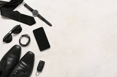 Beyaz arka planda kravat, güneş gözlüğü ve cep telefonu olan erkek aksesuarları. Üst görünüm