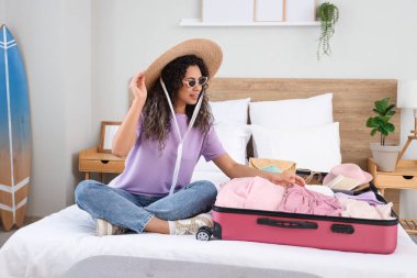 Genç Afro-Amerikalı bir kadın otel odasında bavulunu giysileriyle açıyor.