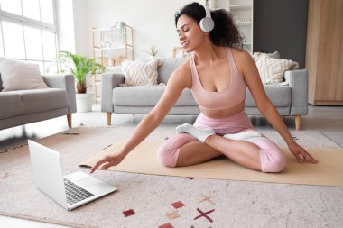 Sportif Afro-Amerikan kadın videosu evde yoga minderinde online antrenörüyle sohbet ediyor.