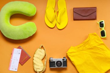 Frame made of travel pillow, photo camera and beach accessories on orange background clipart