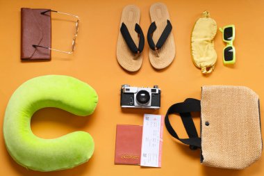 Seyahat yastığı, bilet, pasaport ve turuncu arka planda plaj aksesuarları.