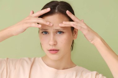 Sivilceleri yeşil arka planda ezen endişeli, güzel bir kadın.